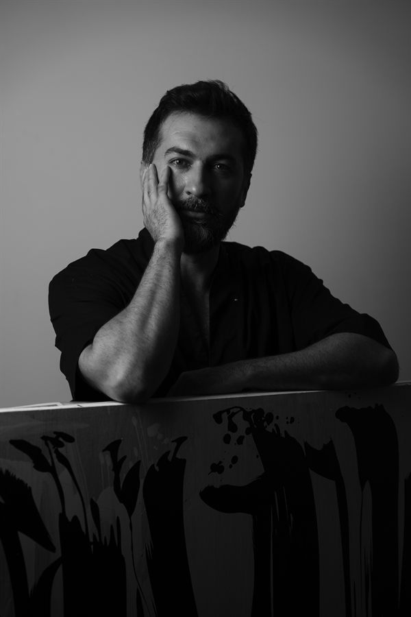 Behnam, leaning against one of his ink-marked canvases